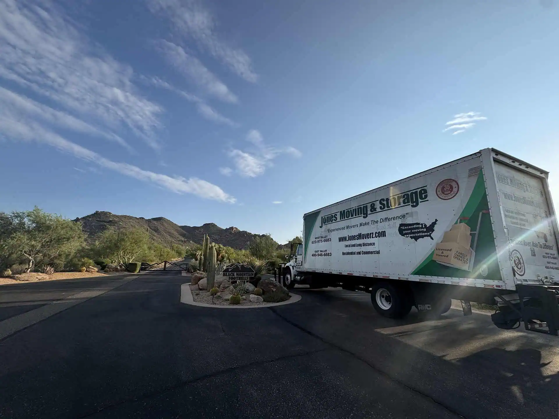 A Jones Moving & Storage box truck at the gated entrance of a desert community, with saguaros and rocky hills behind it